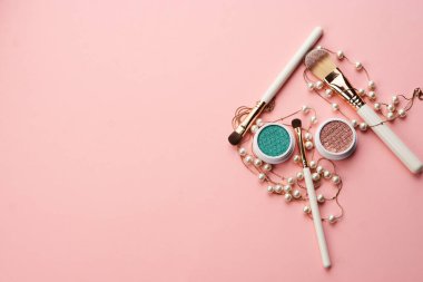 Göz falı aksesuarlar, boncuklar makyaj fırçaları pembe arka planda profesyonel kozmetik ürünleri koleksiyonu.