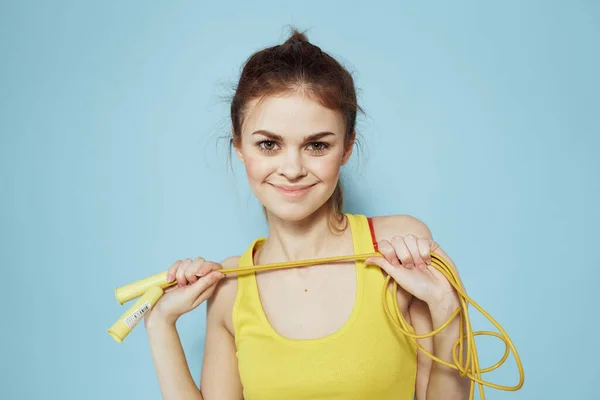 Sportos nő kezében ugrókötél sárga tartály tetején gyakorlat torna kék háttér — Stock Fotó