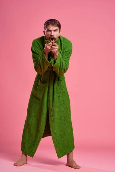 Эмоциональный человек в зеленом халате в полном разгаре на розовом фоне жестикулирует руками к модели — стоковое фото