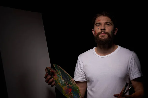 Un homme avec une palette dans ses mains brosse chevalet art Approche créative passe-temps fond sombre — Photo