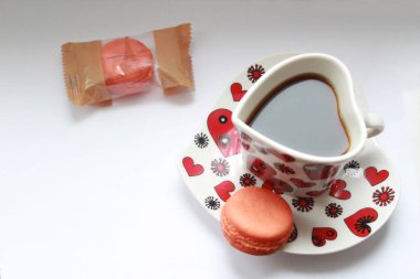 Espresso kahve bir fincan bir uçan daire pasta macaron üzerinde kalp şeklinde renkleri mercan bir pasta macaron paket yakınındaki de. Yatay fotoğraf.