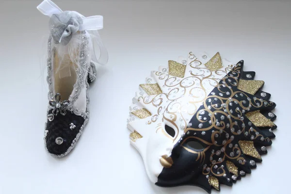 Dekoratif Takı Boncuk ve tüyleri beyaz zemin üzerinde bir maskeyle kil siyah-beyaz ve siyah-beyaz bir ayakkabı. Bir iç süsleme. Şenlikli ruh hali. Yatay fotoğraf.