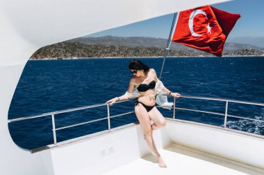 Siyah bikini yatta deniz arka plan üzerinde Turkisf bayrağıyla poz ince kadın
