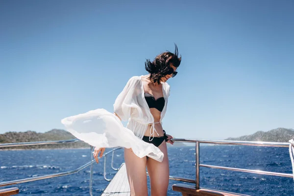 Woman in black bikini posing standing on yacht on sea background