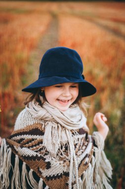 Gülümseyen kız panço ve şapka sonbahar alanı tarafından yürüyüş portresi