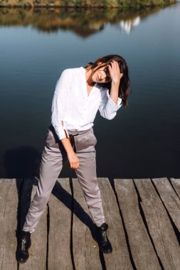 Beyaz gömlek ve gri pantolon iskele, nehir ve sonbahar yaprakları arka plan ayakta poz şık kadın.