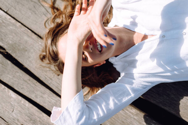 Woman in white shirt laying on wooden pier with lifted arms