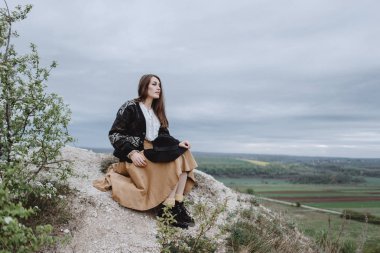 Tepede oturan örgü ceketli genç bir kadın.