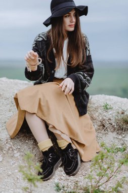 Tepede oturan örgü ceketli ve siyah şapkalı genç bir kadın.