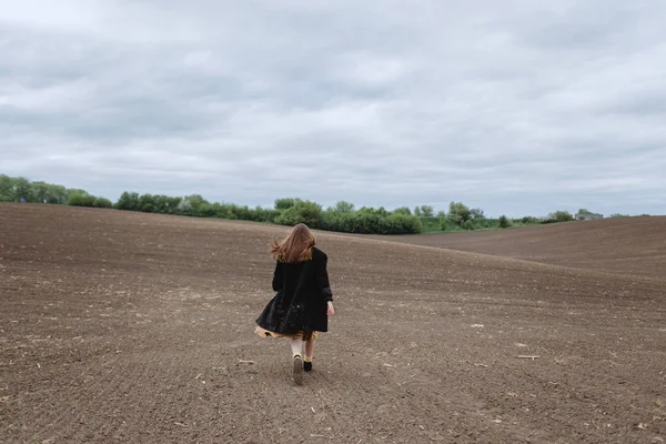 Siyah ceketli kadının sahada yürümesinin arka görünümü