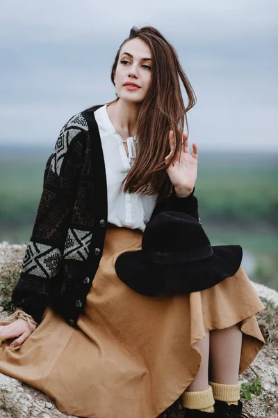 Örgü ceketli genç bir kadın yerde oturmuş saçlarıyla oynuyor.