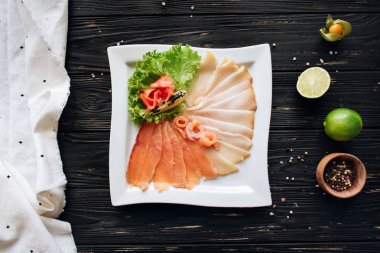 Peppper, limon, beyaz noktalı peçete ile plaka üzerinde dilimlenmiş çeşitli kürlenmiş balık.