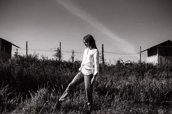 Black and white photo of woman in shirt and pants posing in field