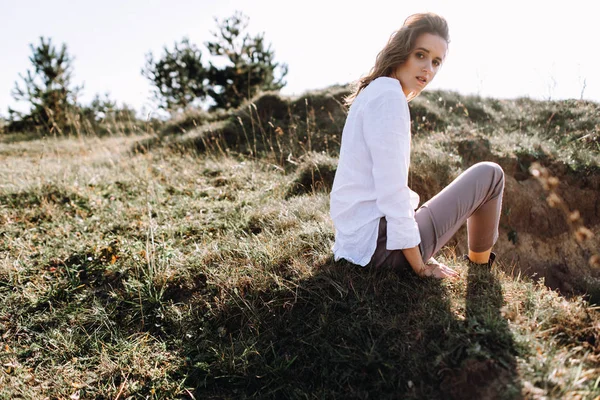 漂亮的女人在衬衫和裤子摆姿势坐在草地上的田野 — 图库照片