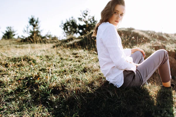 Pretty woman in shirt and pants posing sitting on grass in field