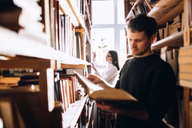 Genç adam ve kadın kütüphanede kitap seçme.