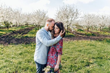 Sevgi dolu çift sarılıyor ve yürüyor. Çiçekli bir elma bahçesinde aşk hikayesi