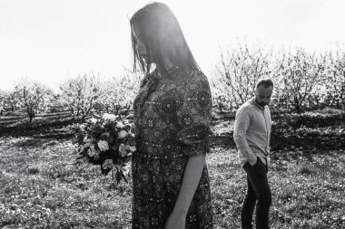 Sevgi dolu çift sarılıyor ve yürüyor. Çiçekli bir elma bahçesinde aşk hikayesi