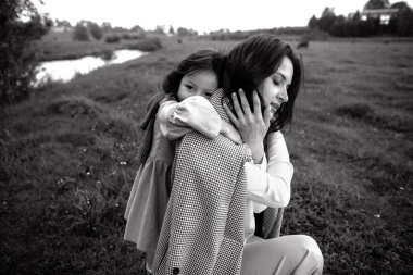 Tarz sahibi anne ve kız yağmur yağdığında nehir kenarındaki yeşil çimlerin olduğu bir arazide eğleniyorlar.