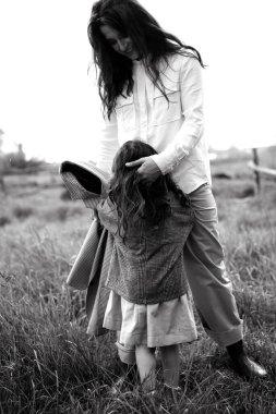 Tarz sahibi anne ve kız yağmur yağdığında nehir kenarındaki yeşil çimlerin olduğu bir arazide eğleniyorlar.