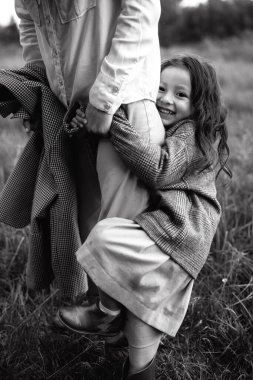 Tarz sahibi anne ve kız yağmur yağdığında nehir kenarındaki yeşil çimlerin olduğu bir arazide eğleniyorlar.