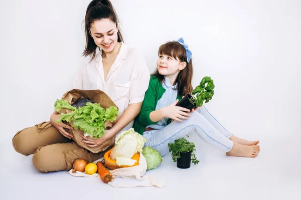 Two Girl unpacking shopping eco bag with vegetables, greens without plastic on white background. Zero waste, plastic free Eco friendly concept.