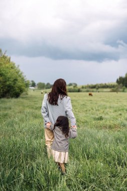 Anne ve kızı yeşil alanda birlikte eğleniyorlar. Gülümseyen anne güzel kızının elini tutuyor.. 