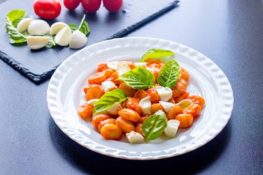 Gnocchi domates soslu Yeşil taze fesleğen ve mozzarella topları ile bir tabakta. İtalyan tarifi
