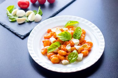 Gnocchi domates soslu Yeşil taze fesleğen ve mozzarella topları ile bir tabakta. İtalyan tarifi