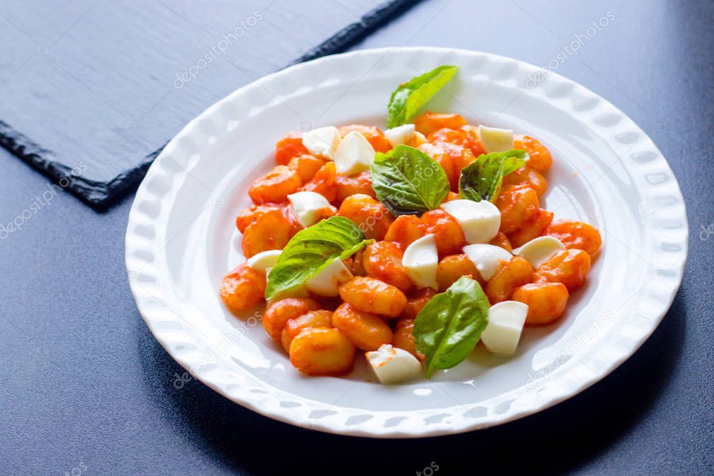 Gnocchi in tomato sauce with green fresh basil and mozzarella balls served on a plate