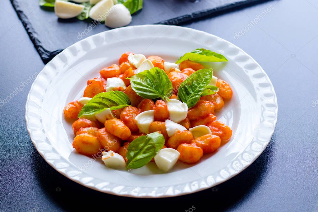 Gnocchi alla Sorrentina in tomato sauce with green fresh basil and mozzarella balls served on a plate