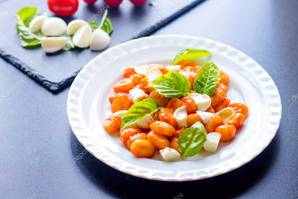 Gnocchi in tomato sauce with green fresh basil and mozzarella balls served on a plate. Italian recipe