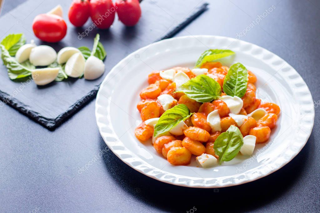 Gnocchi alla Sorrentina in tomato sauce with green fresh basil and mozzarella balls served on a plate