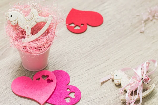 Two rocking ponies toys in pink small bucket and felt hearts flat lay on a wooden background. Top view. Copyspace. Frame