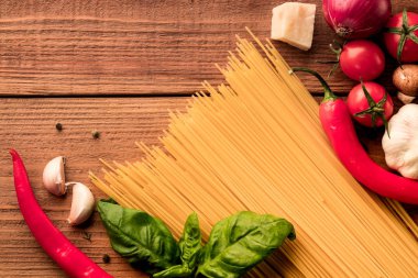 İtalyan Kuru makarna spagetti linguini, taze domates kiraz ile dağınık ahşap arka plan üzerinde kırmızı biber soğuk ve Yeşil fesleğen yaprağı. Üstten görünüm. Boşaltmak. Düz yatıyordu