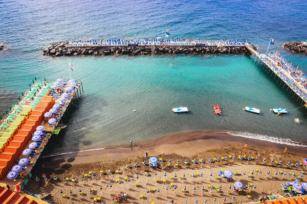 Sorrento summer artificial sand beach with stones of breakwaters on calm blue sea. Italy