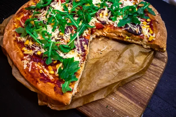 Домашняя пицца с рукколой, сыром пармезан и красным соусом с нарезанным кусочком на пергаменте темный фон, крупным планом — стоковое фото