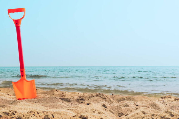 Kid's toy big plastic red and orange shovel stuck in a white sand at the beach sea shore on sunny Summer day. Vacation with children in Italy, Tyrrhenian sea, Pontecagnano, Campania.
