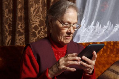 Kanepesinde oturan e-kitap okuyan çok yaşlı bir kadın.