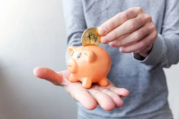 Piggy bank, hand holds golden bitcoin coins virtual money. Cryptocurrency and saving concept