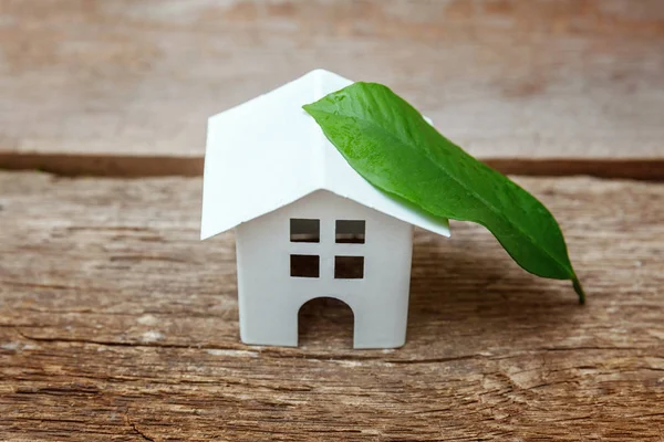 Miniature white toy model house with green leaves on wooden backgdrop. Eco Village, abstract environmental background. Real estate mortgage property insurance dream home ecology concept