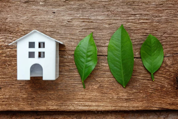 Miniature white toy model house with green leaves on wooden backgdrop. Eco Village, abstract environmental background. Real estate mortgage property insurance dream home ecology concept