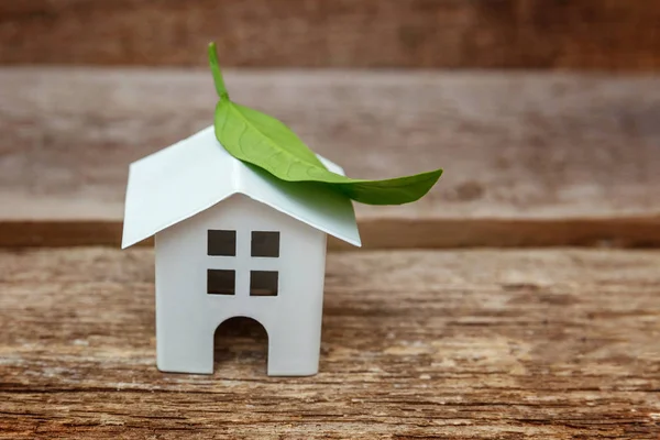 Miniature white toy model house with green leaves on wooden backgdrop. Eco Village, abstract environmental background. Real estate mortgage property insurance dream home ecology concept