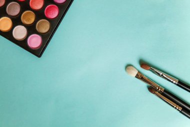 Makyaj ve kozmetik farklı tonları göz farı paleti ve mavi arka plan üzerinde fırçalar makyaj için araçlar. Renkli kozmetik mavi çalışma alanı üzerinde. Üstten görünüm düz yatıyordu ve pitoresk