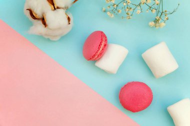 Üstten görünüm mini pembe macaron veya acıbadem kurabiyesi Fransız marshmallow ile tatlılar pasta ve pamuk yumuşak tatlı pembe ve mavi pastel geometrik çiçekler kağıt düz yatıyordu arka plan.