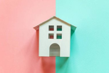 Minyatür beyaz oyuncak evi pembe ve mavi pastel renkli kağıt geometrik trendy arka plan üzerinde sadece düz yatıyordu tasarım. Mortgage Emlak sigorta rüya ev concept