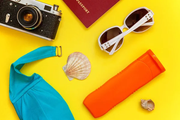 Düz Lay Bikini, çınar, bağbozumu kamera, pasaport, Güneş kremi, güneş gözlüğü ve kabuk üzerinde sarı renkli şık modern moda arka plan ile. Tatil seyahat yaz hafta sonu deniz macera seyahat kavramı