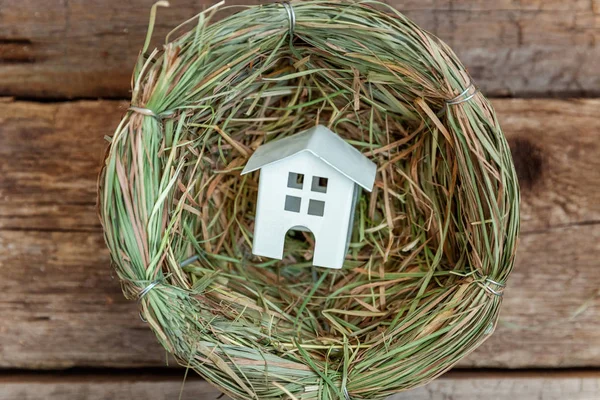 Miniature white toy model house rests in nest on rustic old vintage wooden background. Eco village environmental real estate mortgage property insurance dream home ecology investment concept