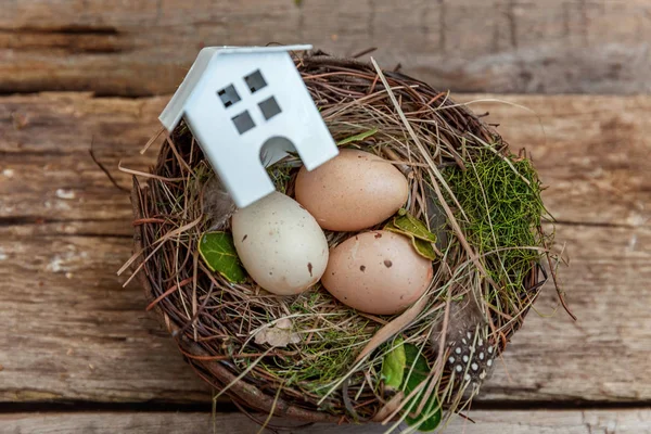 Minyatür beyaz oyuncak model house rustik eski vintage ahşap arka plan üzerinde yumurta yuvada aittir. Eko köyü çevre gayrimenkul ipotek Emlak sigorta rüya ev ekoloji yatırım kavramı