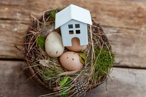 Minyatür beyaz oyuncak model house rustik eski vintage ahşap arka plan üzerinde yumurta yuvada aittir. Eko köyü çevre gayrimenkul ipotek Emlak sigorta rüya ev ekoloji yatırım kavramı
